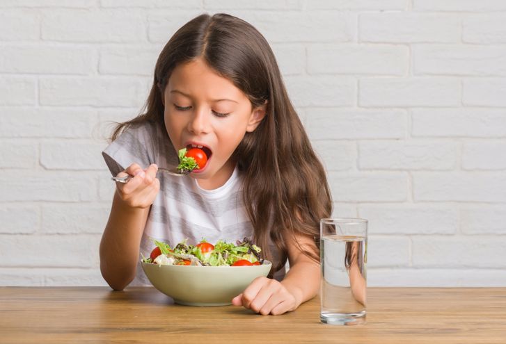 Kind isst einen grünen Salat mit Tomaten