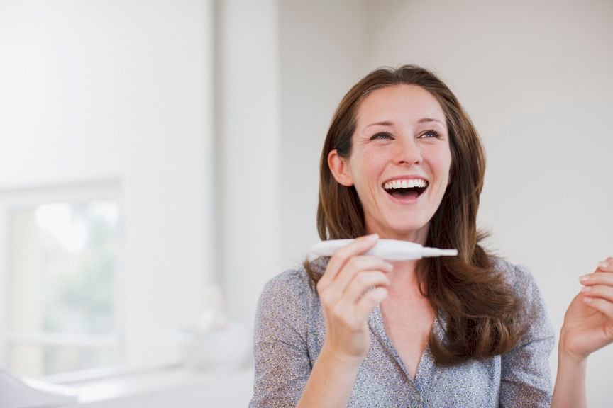 Frau hält lächelnd einen Schwangerschaftstest in der Hand