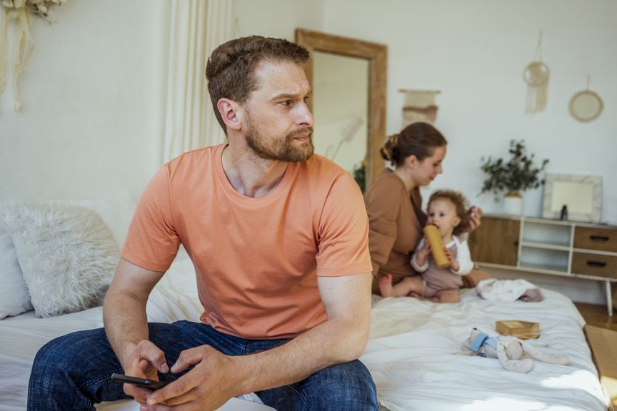 Vater nachdenklich, Mutter mit Baby im Hintergrund