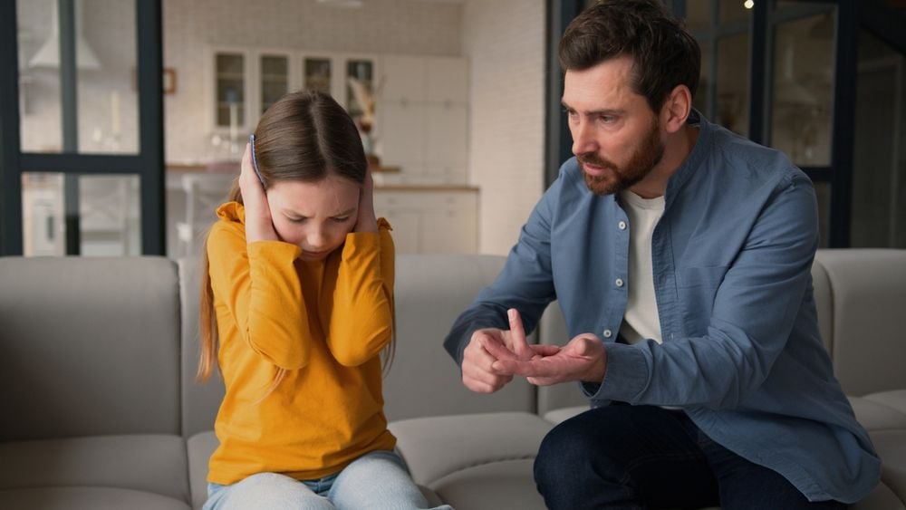 Mann schimpft mit Kind, das sich die Ohren zuhält