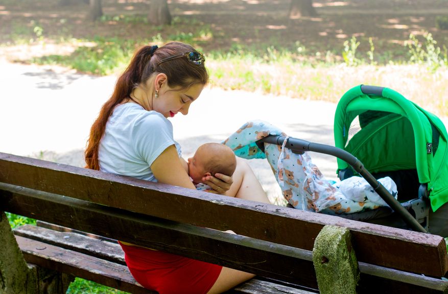 Frau sitzt auf einer Parkbank und stillt ihr Baby