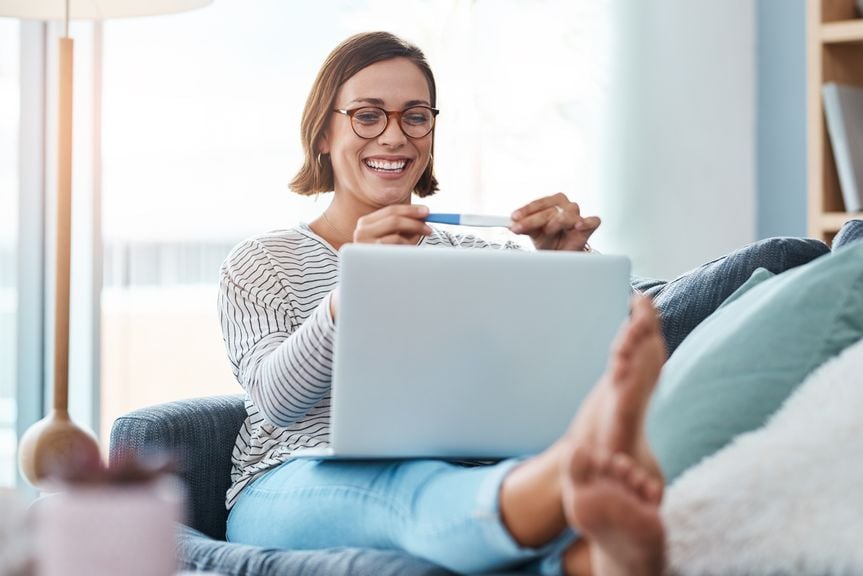 Frau mit Schwangerschaftstest und Laptop strahlt