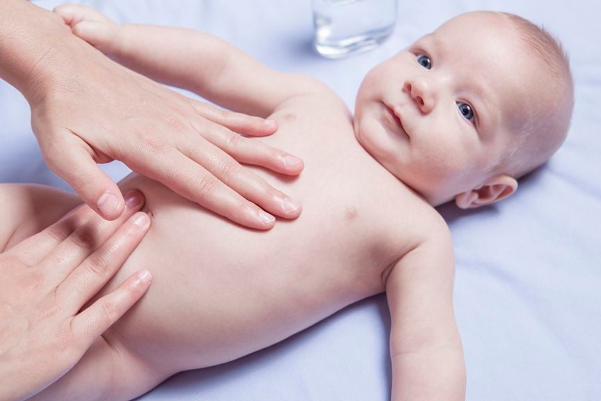 zwei Hände auf Babys Bauch machen Bauchmassage
