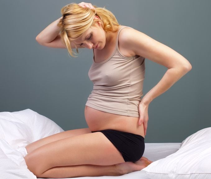 Schwangere kniet auf dem Bett und hält sich den Rücken