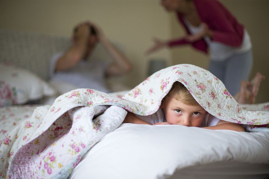 Kind verkriecht sich unter der Decke, während die Eltern streiten