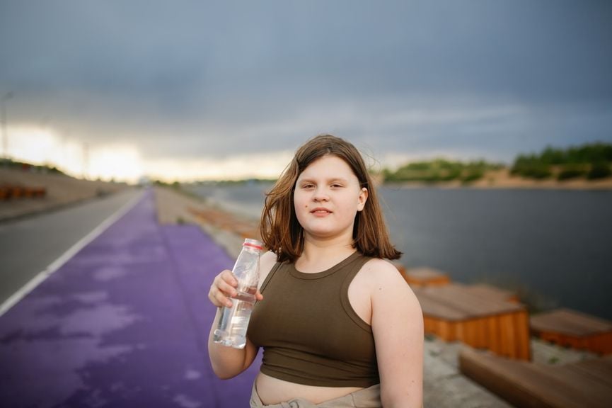 Übergewichtiges Kind mit einer Wasserflasche macht Pause beim Sport