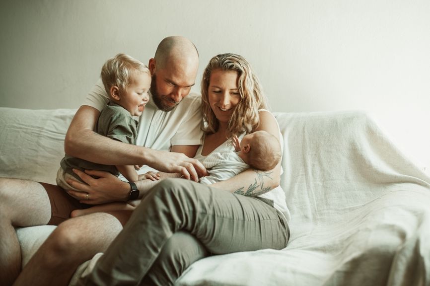 Eltern sitzen mit Neugeborenem und Kleinkind auf dem Sofa