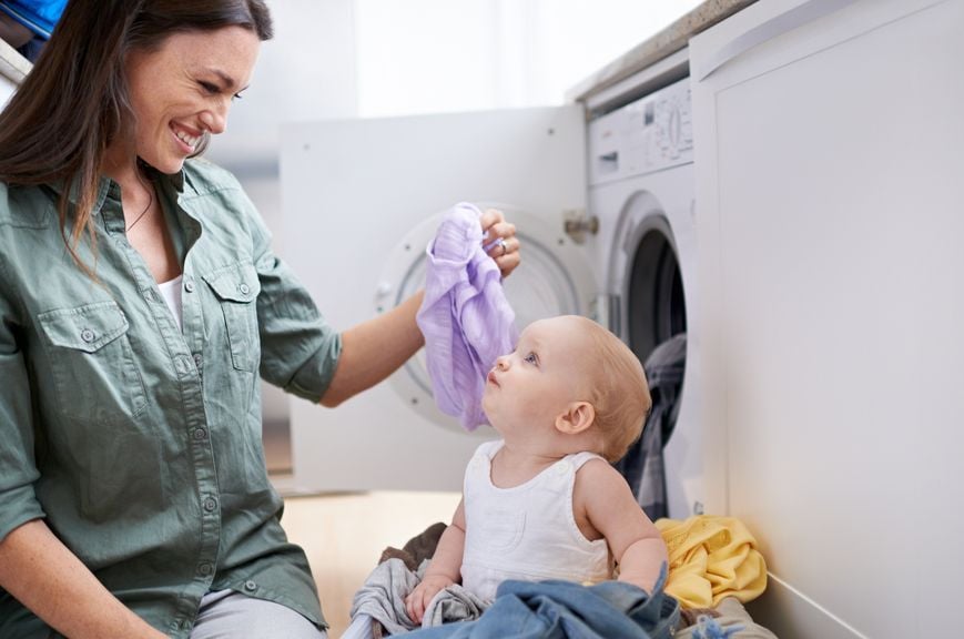 Mutter und Baby mit Wäsche vor der Waschmaschine