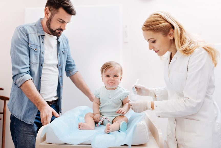 Baby erhält von Ärztin eine Impfung, Vater steht daneben
