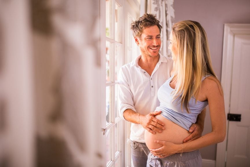 Werdender Vater legt seine Hand auf den Bauch seiner schwangeren Frau