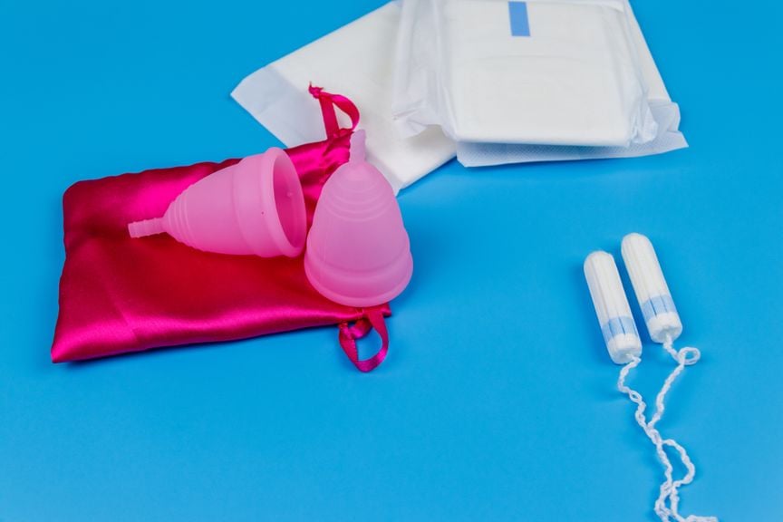 Menstruationstassen, Damenbinden und Tampons vor blauem Hintergrund