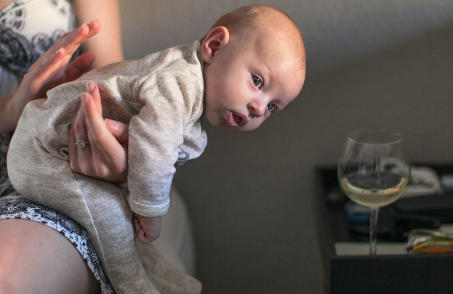 Teilansicht einer Frau mit einem Säugling auf dem Schoss; hält die Hand über dem Babyrücken