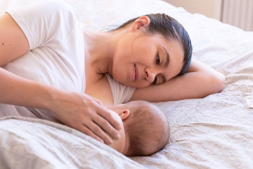 Mutter stillt ihr Neugeborenes im Bett
