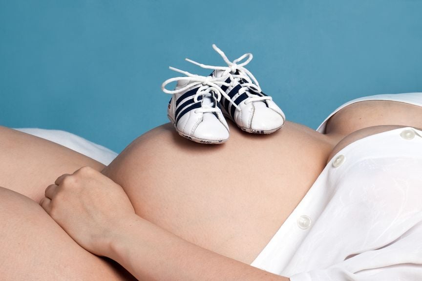 liegende Schwangere mit Schühchen auf dem Bauch