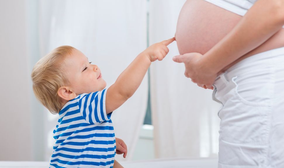 Kind tippt mit dem Finger auf den Babybauch seiner Mutter