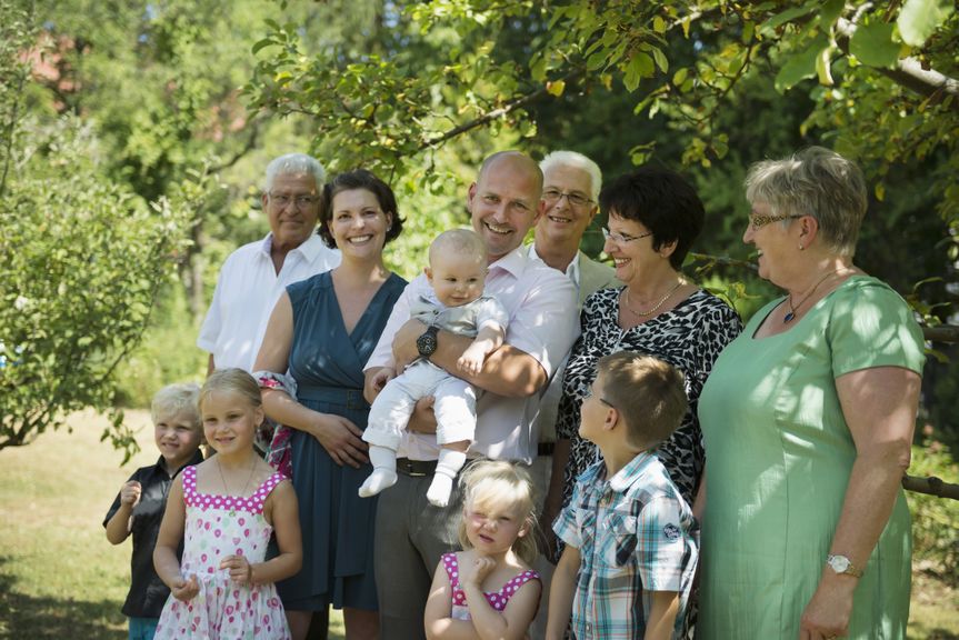 Mehrgenerationenfamilie posiert mit einem Baby unter einem Baum für ein Foto
