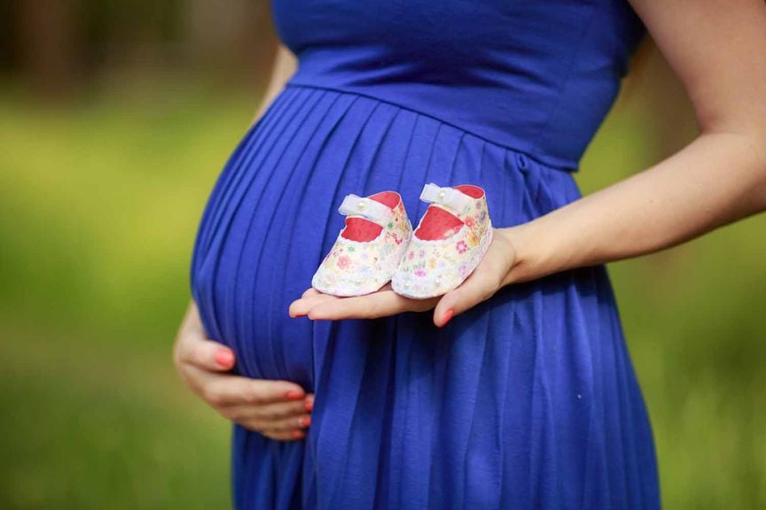 Schwangere im blauen Kleid mit Babyschuhen