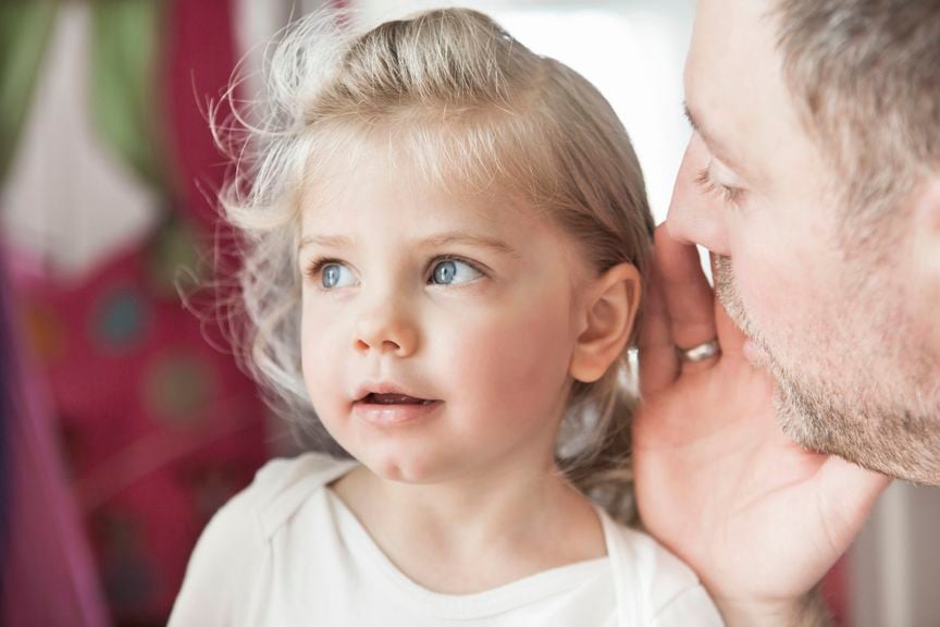 Vater flüstert Tochter etwas ins Ohr