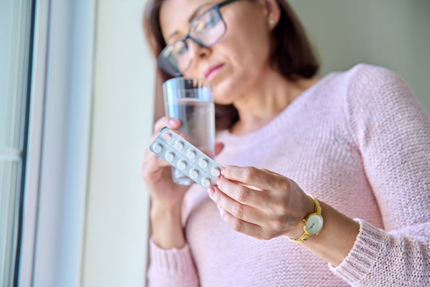 Frau mit Wasserglas und Medikamenten