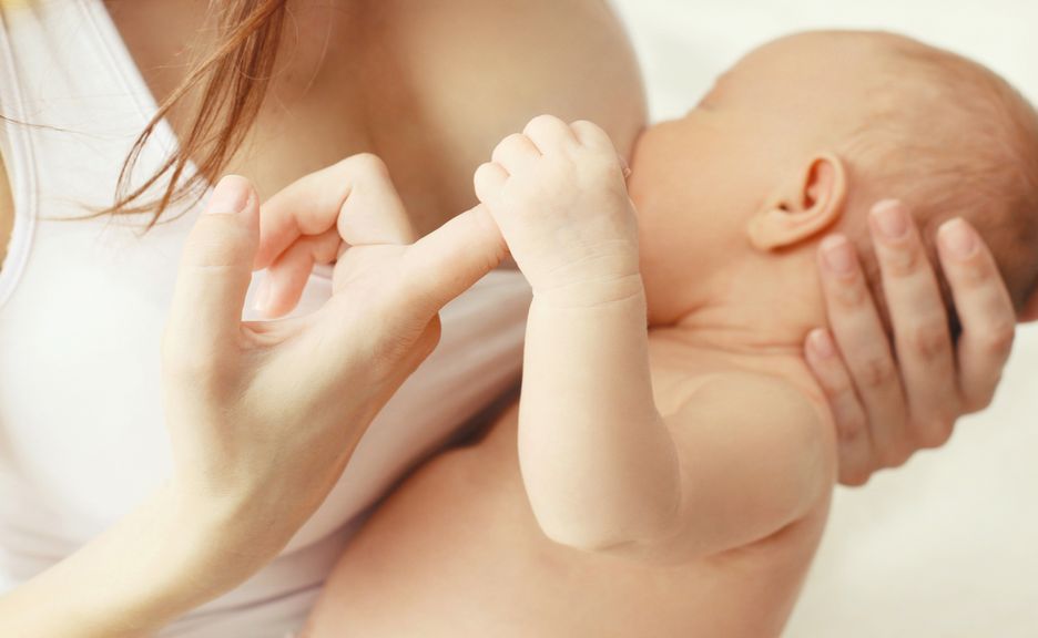 Baby trinkt an der Brust und hält Mutters Zeigefinger fest