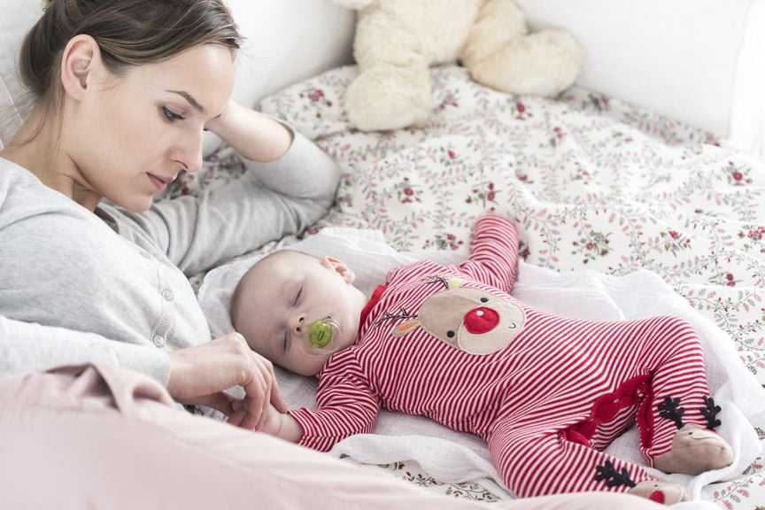 Mutter liegt neben dem schlafenden Baby und streichelt seine Hand