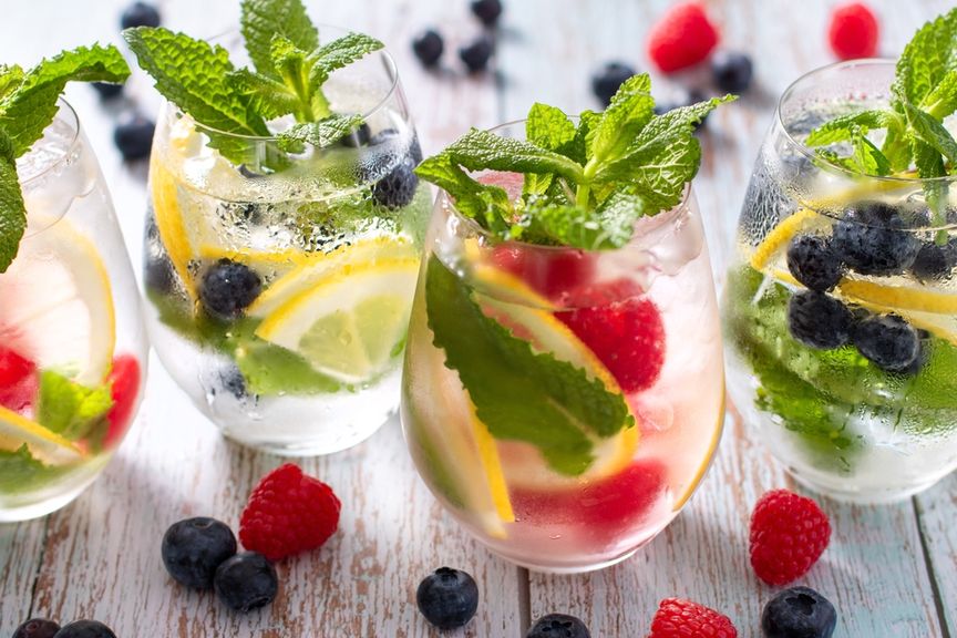 Wassergläser mit Beeren, Zitronenschnitzen und Kräutern.