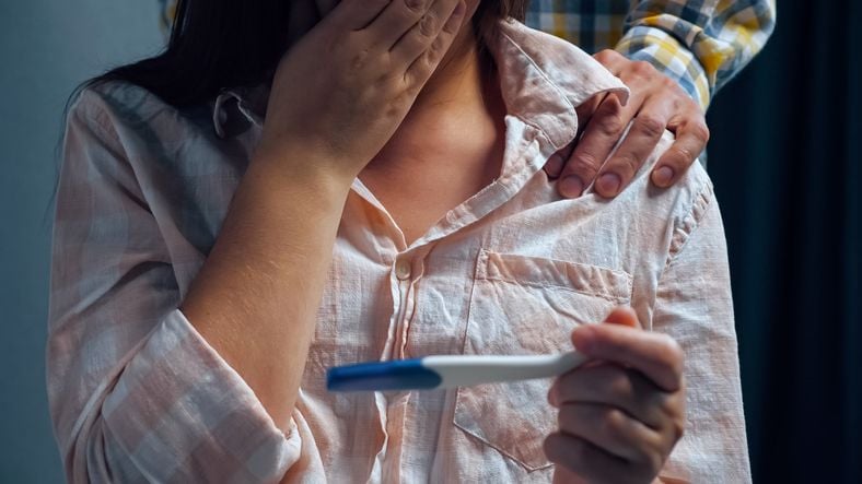 Frau mit Schwangerschaftstest hält sich die Hand vor den Mund