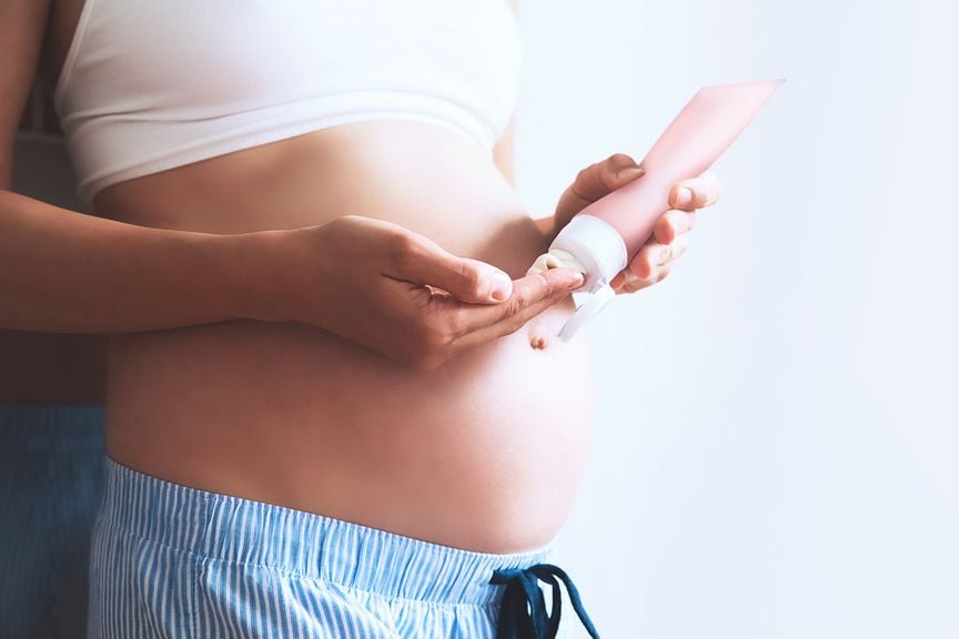 Schwangere entnimmt Creme aus einer Tube zur Hautpflege des Babybauches,Schwangere mit Creme für den Babybauch