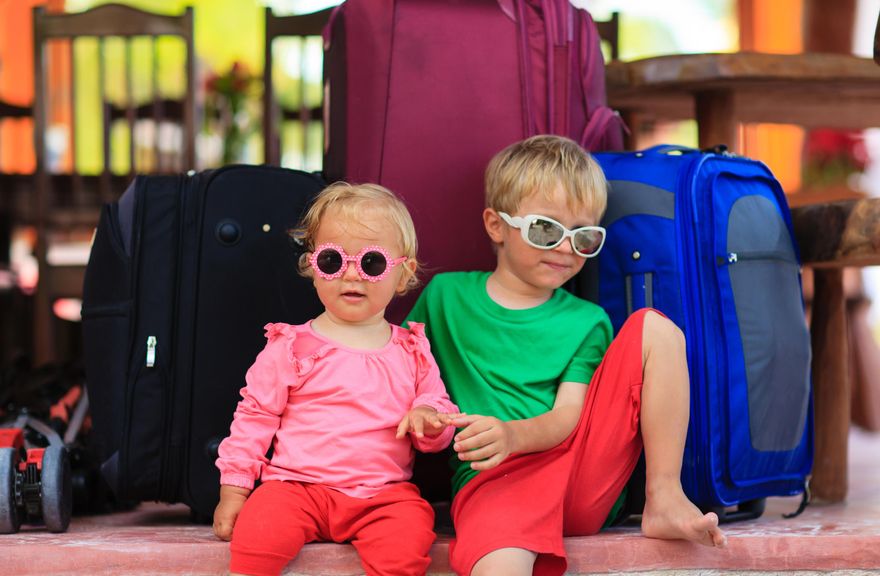 Geschwister sitzen vor gepackten Koffern 