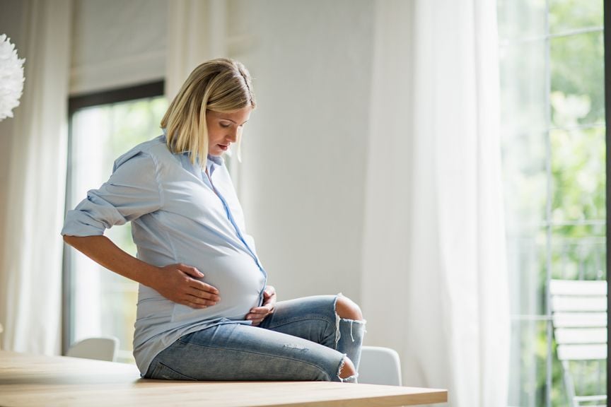 Schwangere sitzt auf dem Tisch und hält sich den Bauch