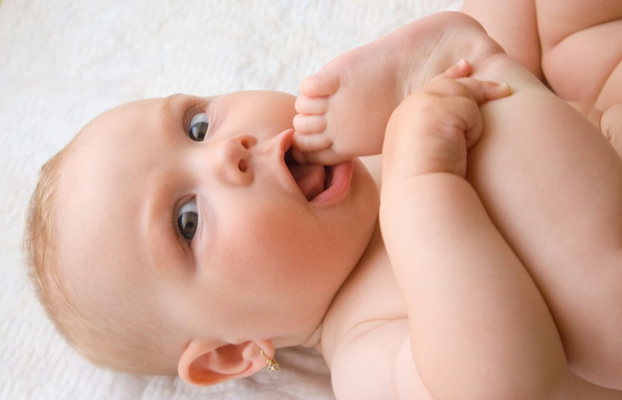 nacktes Baby nimmt seinen Zeh in den Mund. iStock. ©. 