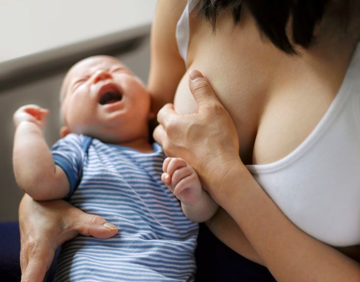 Mutter hält sich die Brust, Baby weint