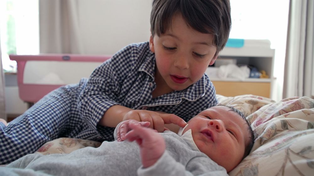 Grosses Kind streicht dem neugeborenen Geschwister mit dem Finger über die Wange