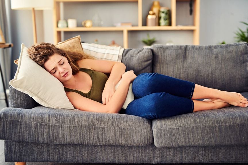 Frau liegt auf dem Sofa mit Wärmflasche auf dem Bauch