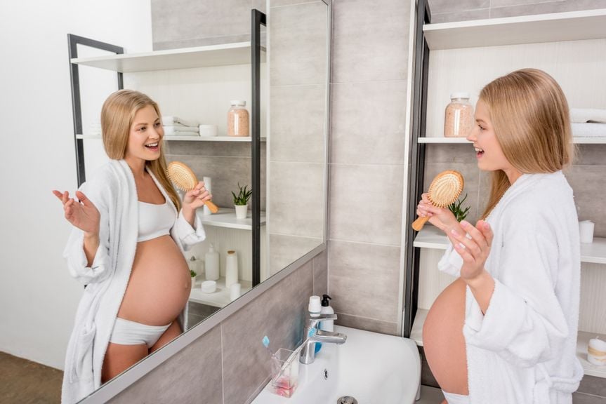 Schwangere lächelt sich im Spiegel an
