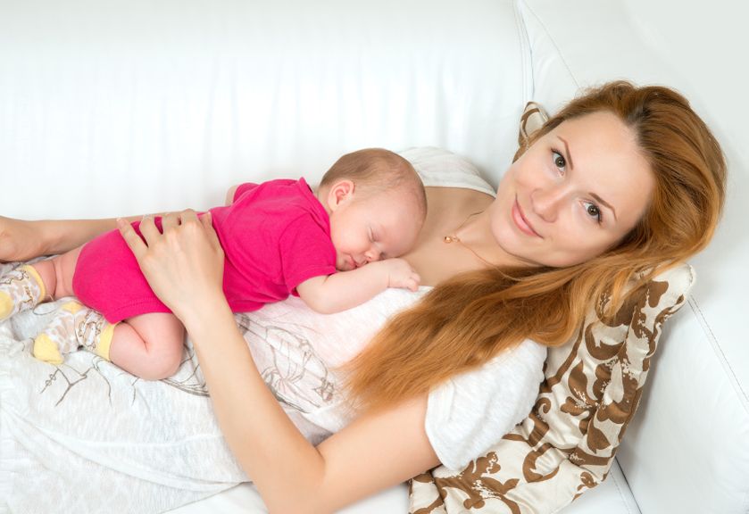 Mutter liegt auf dem Sofa mit Baby auf dem Bauch