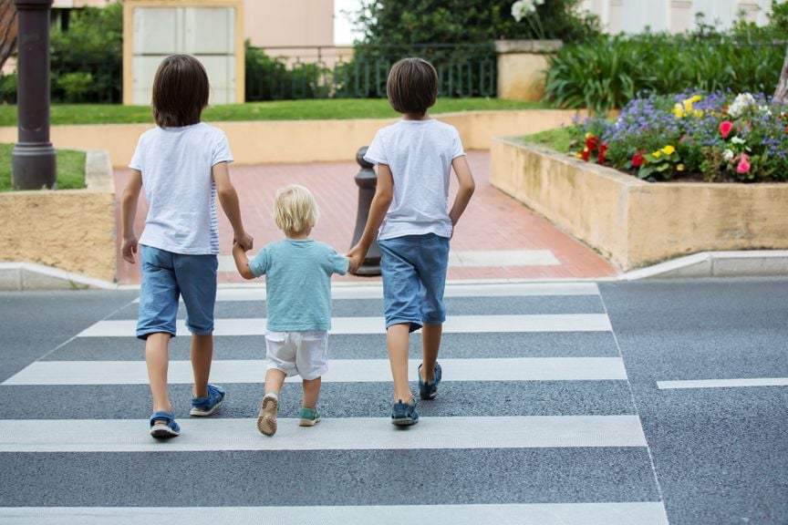 Drei Kinder überqueren einen Fussgängerstreifen