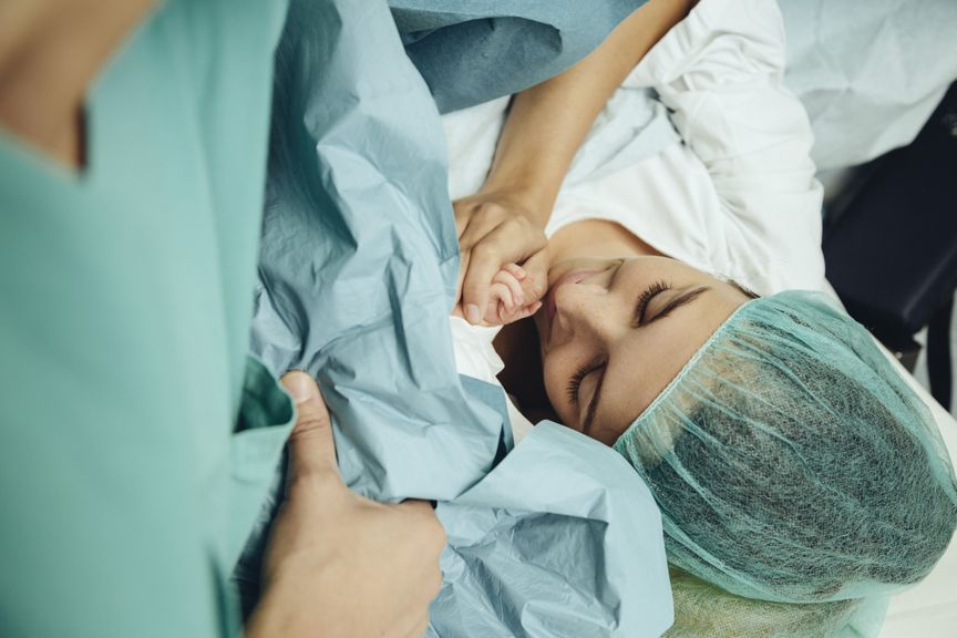 Mutter hält die Hand ihres Neugeborenen direkt nach dem Kaiserschnitt