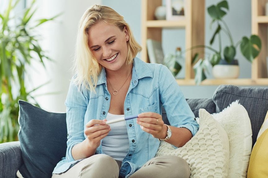 Frau auf dem Sofa mit positiven Schwangerschaftstest