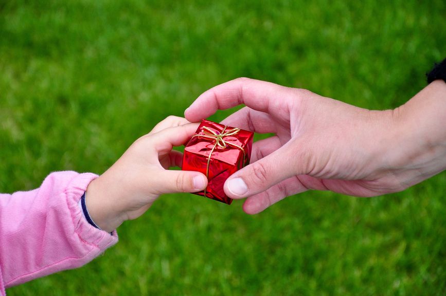 Kinderhand gibt ein kleines Geschenk an eine Frauenhand