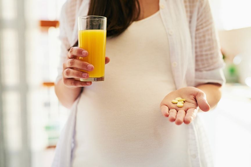 Schwangere nimmt Medikamente mit einem Glas Orangensaft