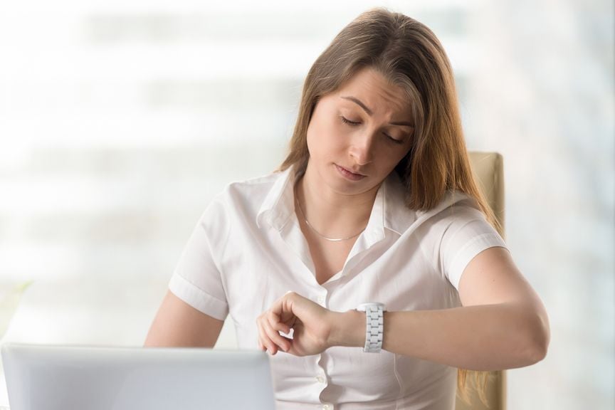 Frau am Laptop schaut auf die Uhr