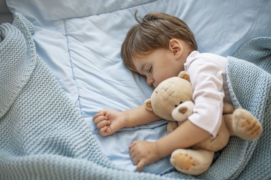 Kind liegt mit seinem Teddy tagsüber im Bett