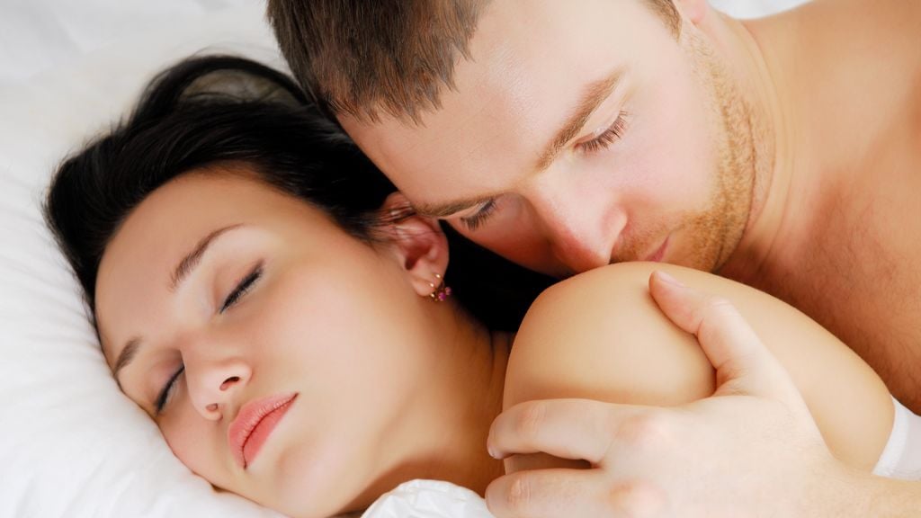 Paar im Bett, sie schläft, er küsst sie auf die Schulter