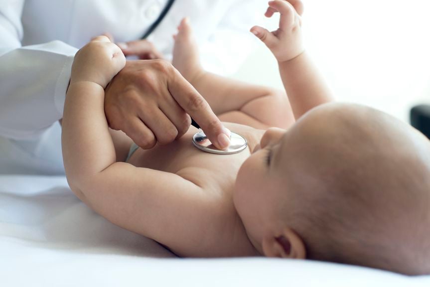 Kinderarzt hält Stethoskop auf die Babybrust