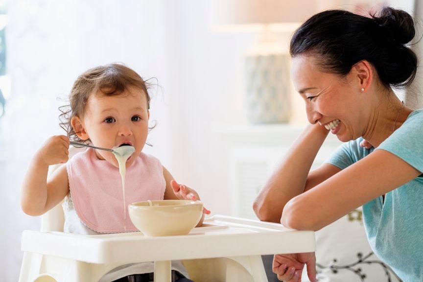 Kind kleckert mit Essen, Mutter lacht