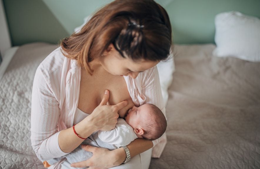 Mutter auf dem Bett sitzend stillt ihr Baby