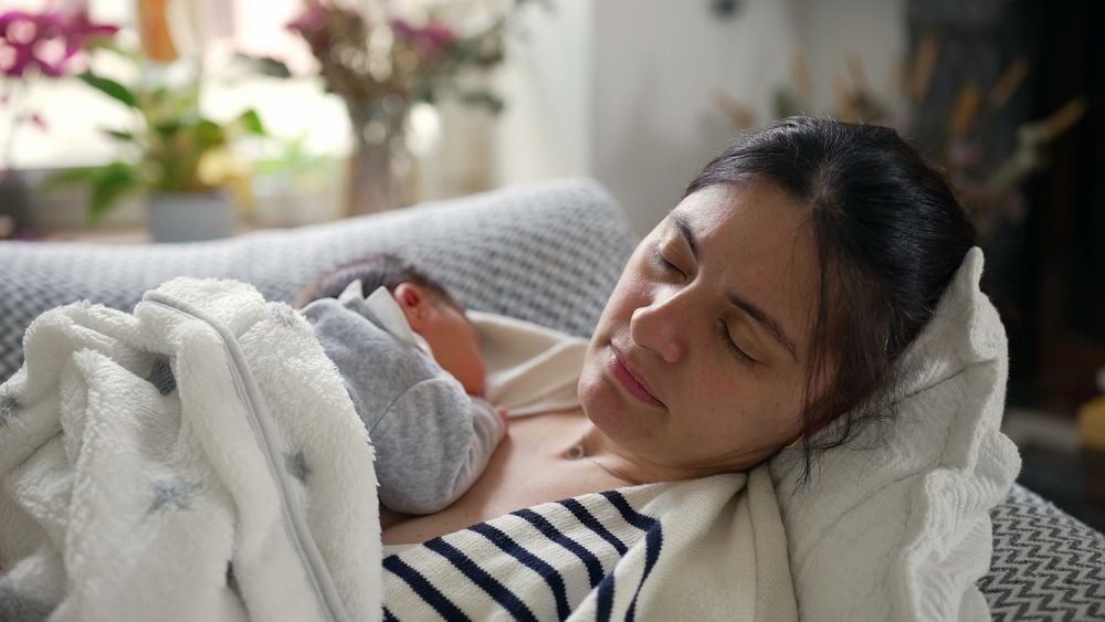 Mutter mit einem Neugeborenen schläft auf dem Sofa