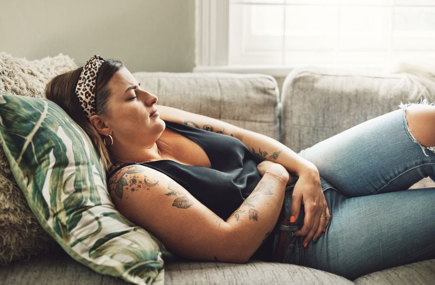 Junge Frau mit Mensturationsschmerzen (Endometriose) auf dem Sofa