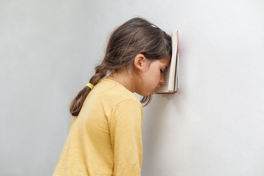 Mädchen dürckt Buch mit Stirn an die Wand